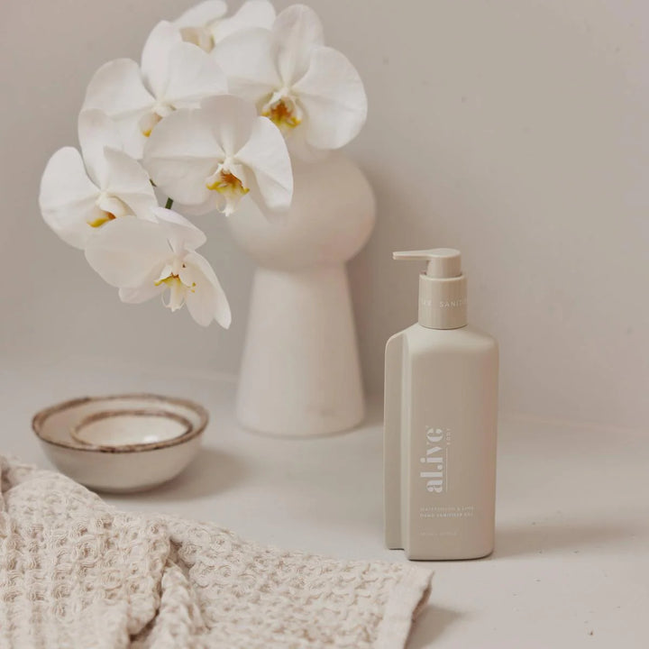 Skincare bottle labeled 'alive' next to a vase with white flowers on a neutral background