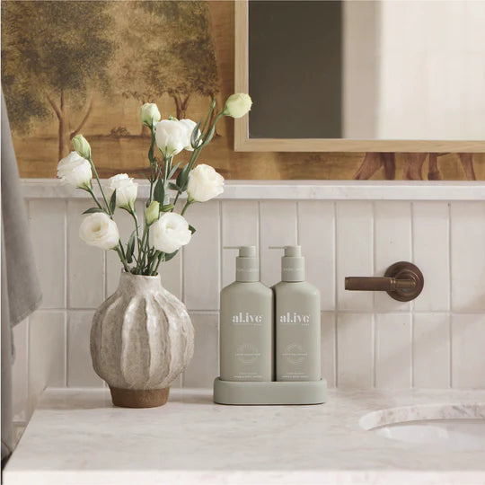 Bathroom counter with 'alive' bottles, a vase with white flowers, and a mirror.