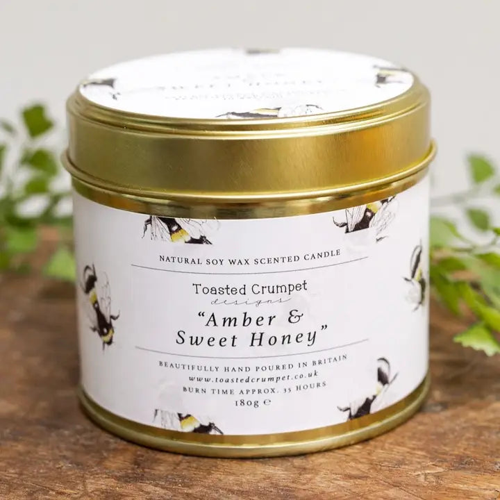 Scented candle in a tin with a decorative label on a wooden surface.