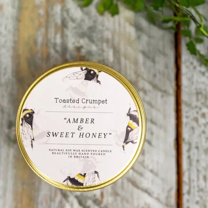 Candle packaging with bee illustrations and 'Amber & Sweet Honey' text on a wooden background