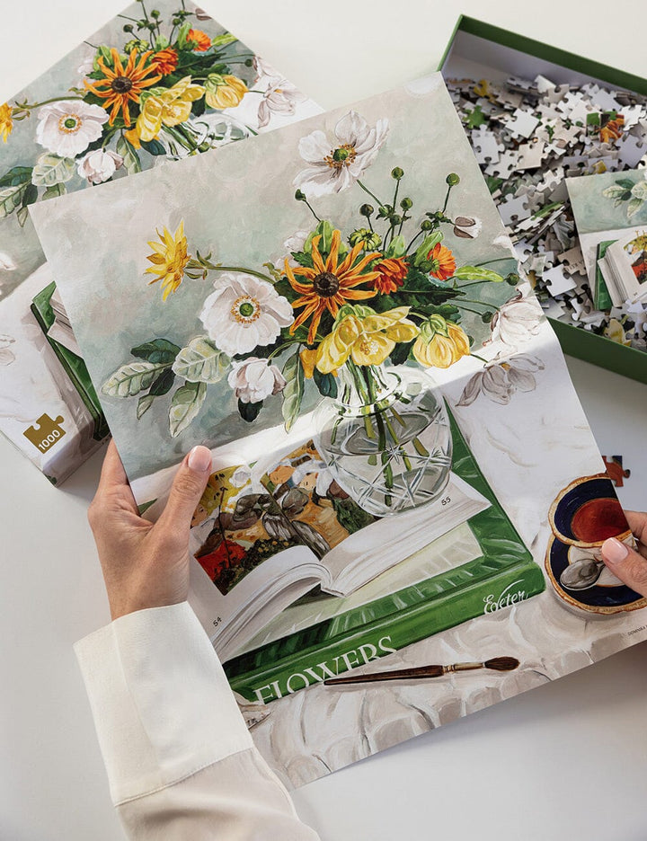 Floral-themed puzzle with a hand holding a piece, on a white surface.