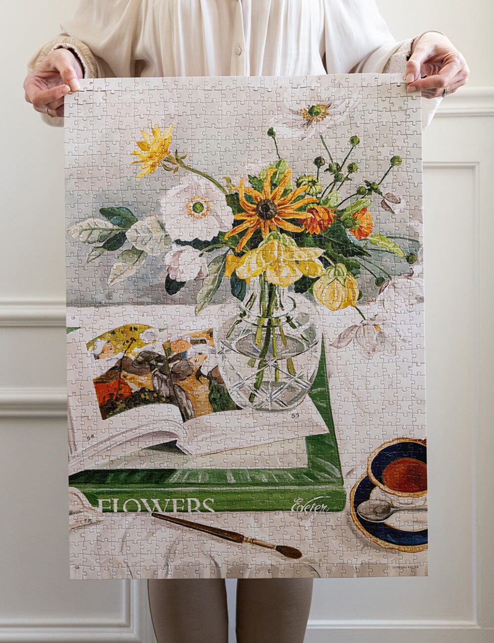 Person holding a large puzzle with a floral design on a white wall.
