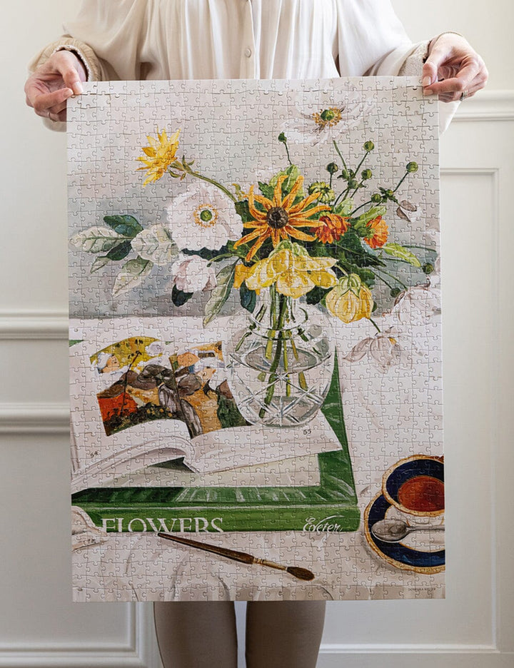 Person holding a large puzzle with a floral design on a white wall.