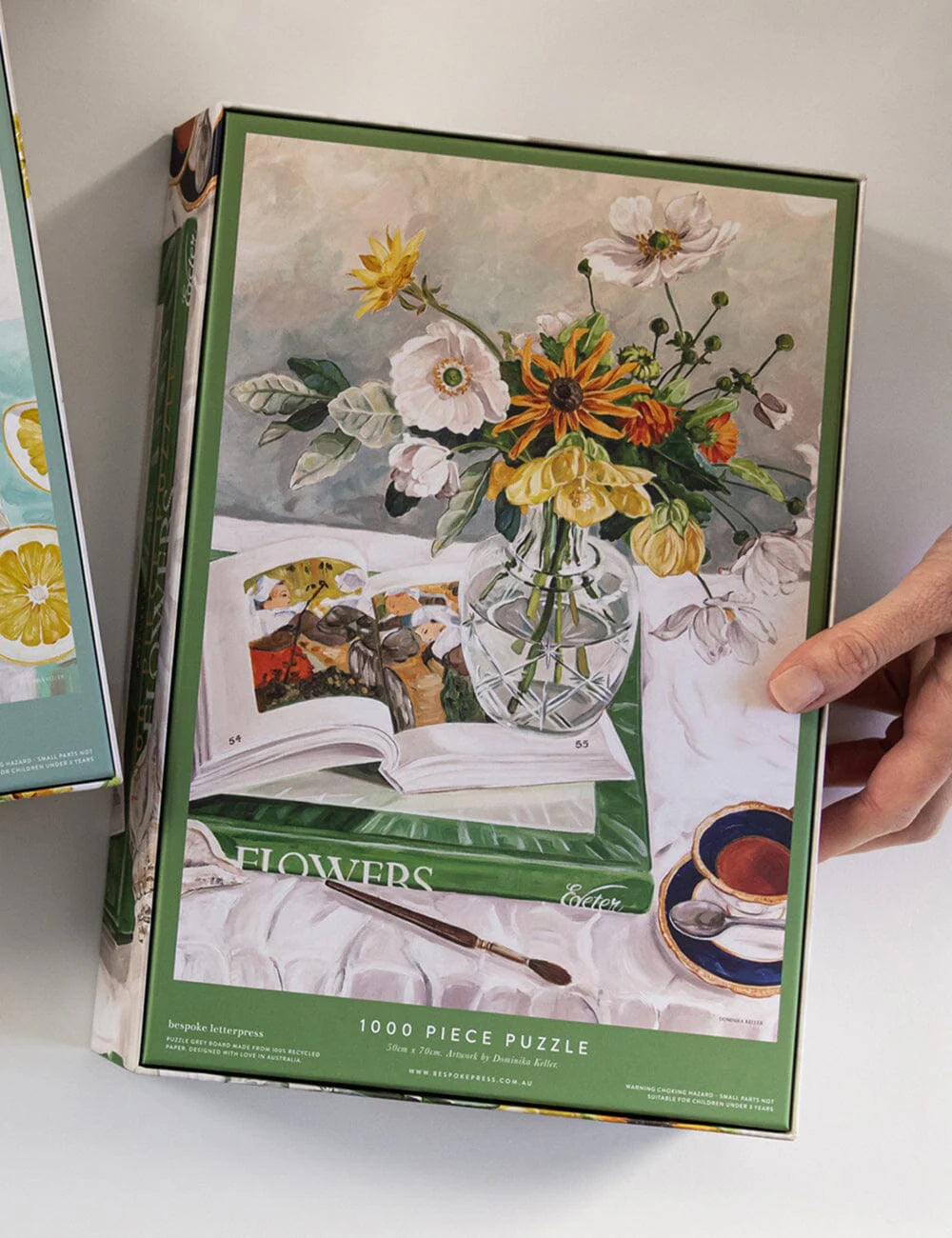 Floral-themed puzzle box with a hand holding it on a light background