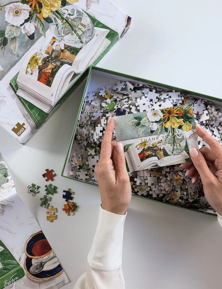 Person assembling a puzzle with floral-themed cards on a white surface
