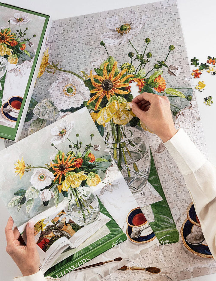 Person assembling a floral-themed puzzle with a completed section on a table.
