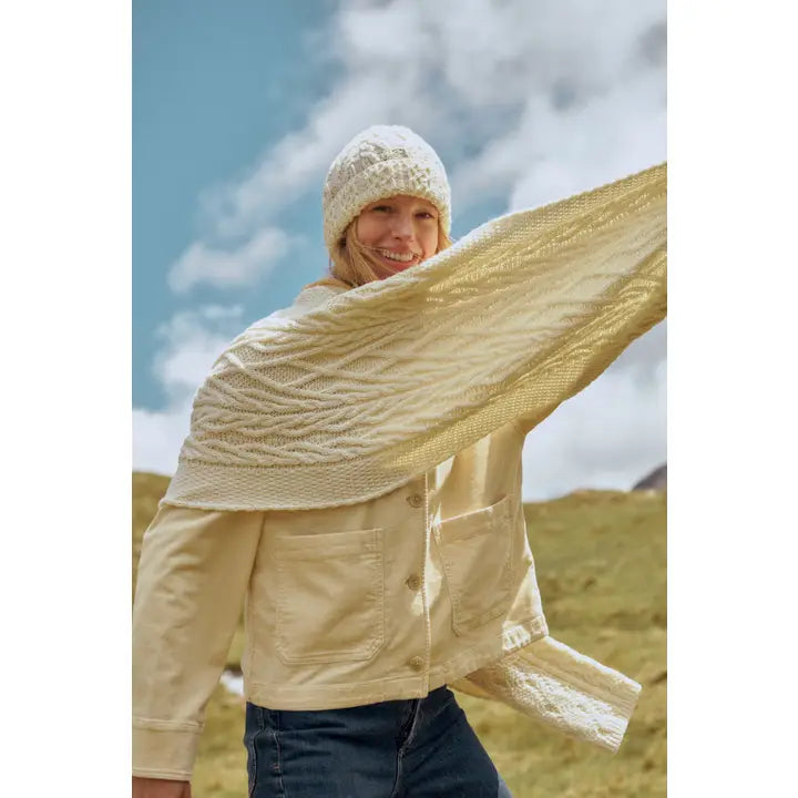 Person wearing a beige knitted shawl and hat outdoors with a blue sky.