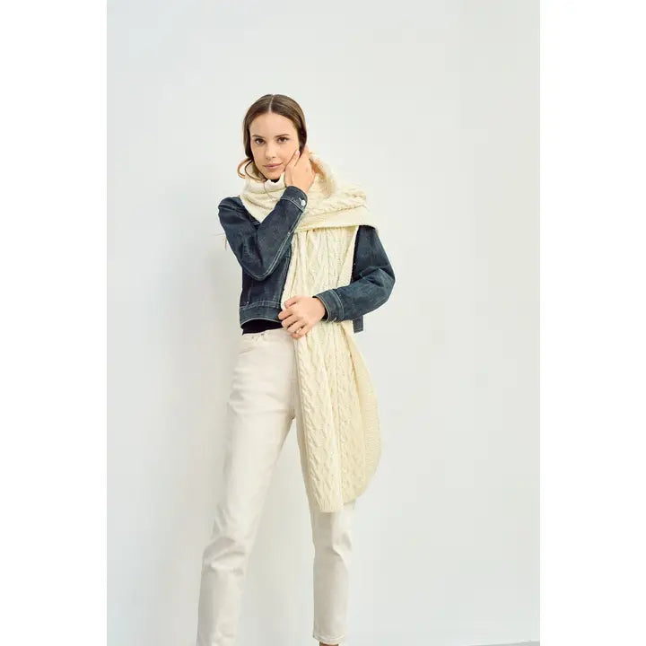 Woman wearing a white cable knit sscarf and cream pants & a denim jacket against a white background