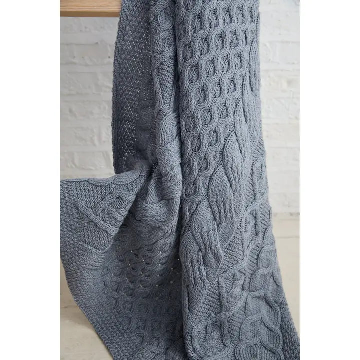 Gray knitted blanket with cable pattern draped over a wooden surface.