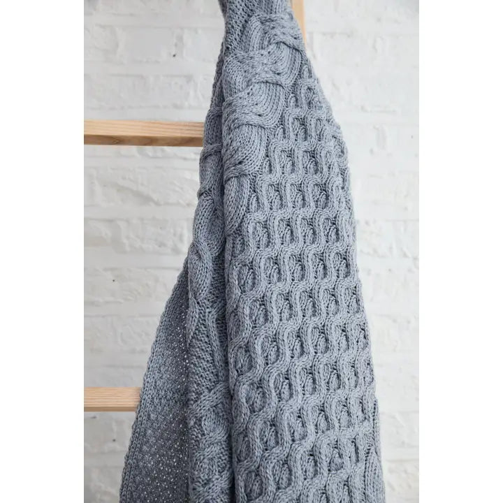Gray Blue knitted blanket draped over a wooden rack against a light gray wall.