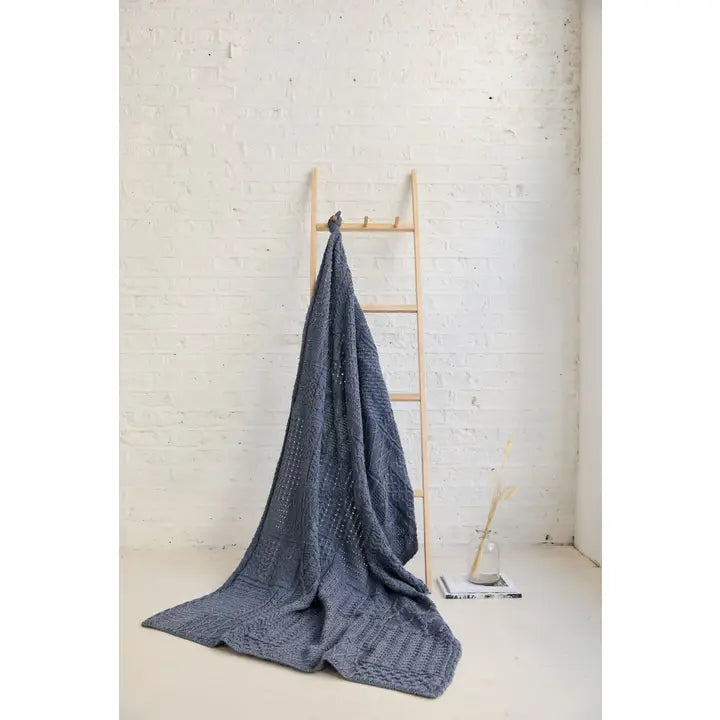 Blue knitted blanket draped over a wooden ladder against a white brick wall.