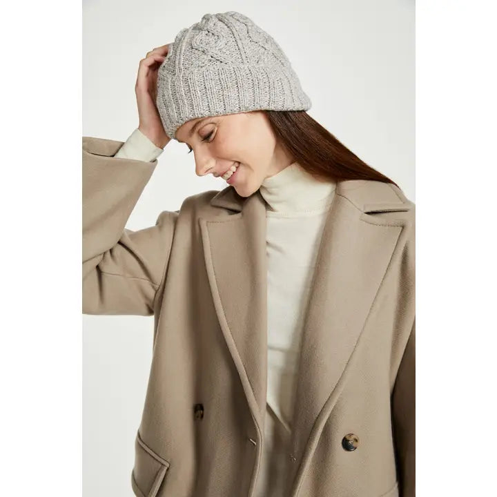 Woman wearing a beige coat and gray knit beanie on a white background
