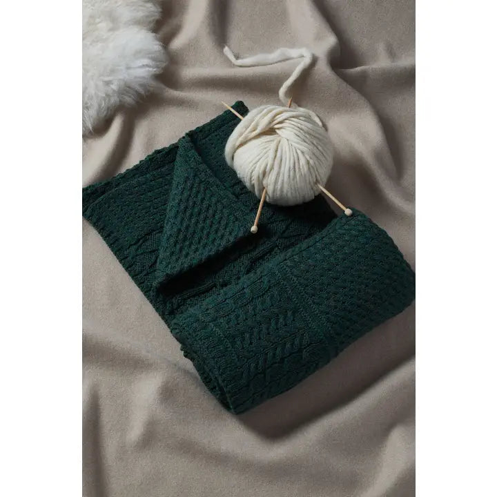 Green knitted blanket with a ball of white yarn on a beige surface