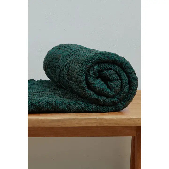 Rolled-up green blanket on a wooden surface with a light gray background