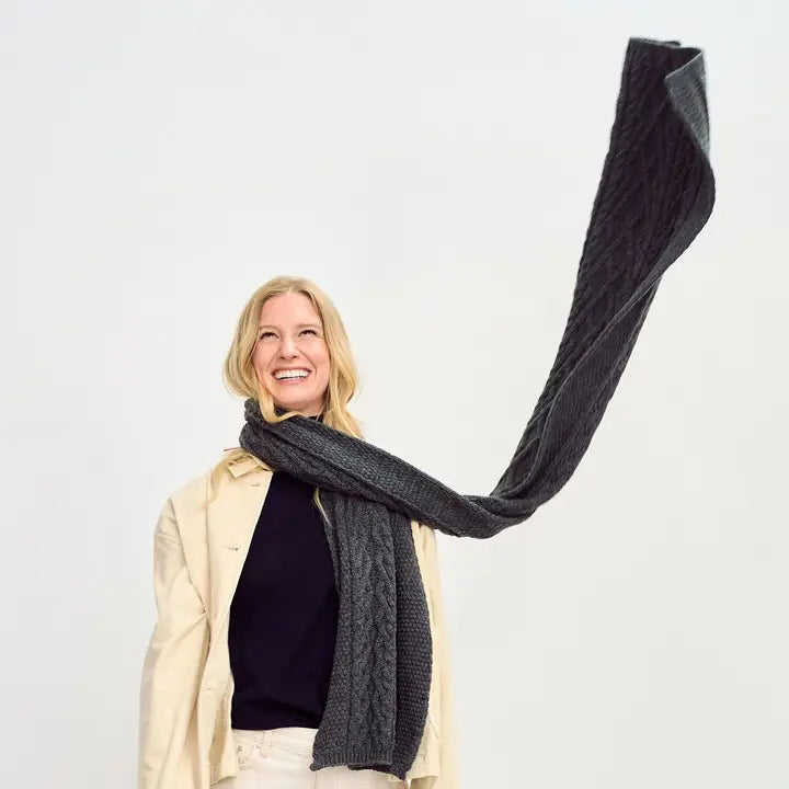 Person wearing a long dark gray scarf against a white background