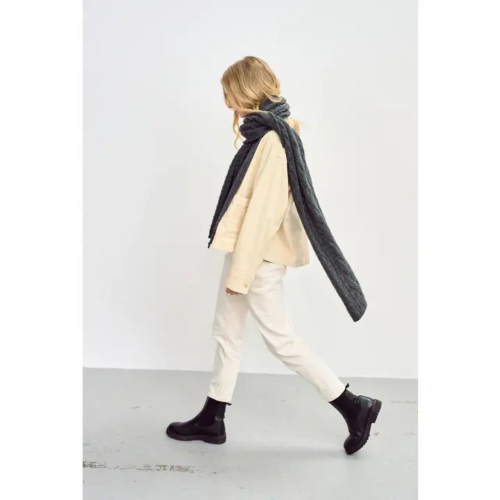 Person wearing a long dark gray scarf in a minimalistic setting