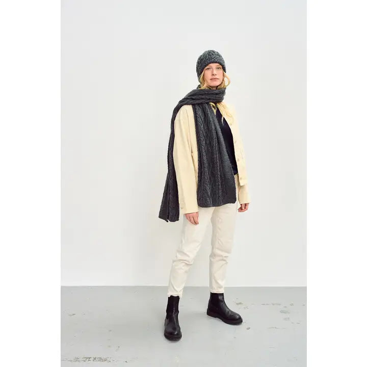 Person wearing a grey scarf, beige shirt, white pants, and black boots on a white background