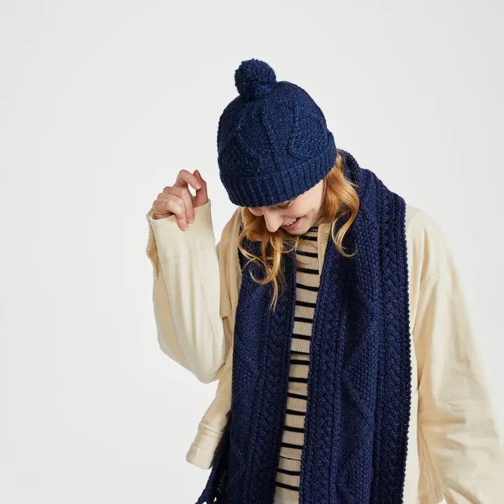 Person wearing a navy blue knitted hat and scarf on a white background