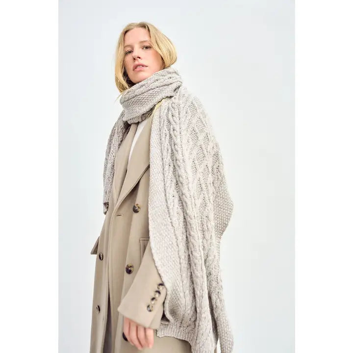 Woman wearing a large knitted scarf and coat on a plain background