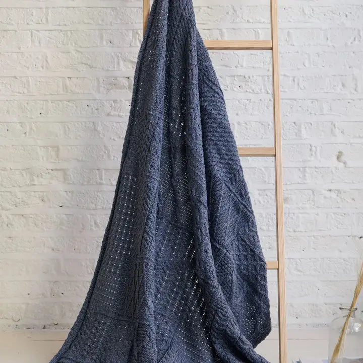 Dark blue textured blanket draped over a wooden ladder against a light brick wall.