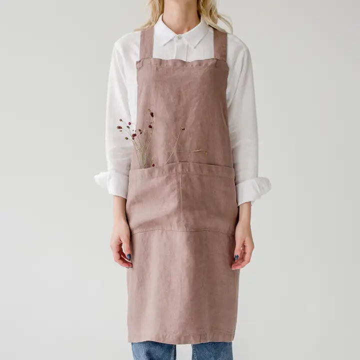 Person wearing a rose coloured apron over a white shirt on a plain background