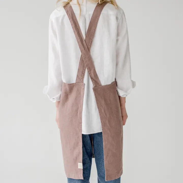 Person wearing a long pink apron over a white shirt and blue jeans on a light gray background