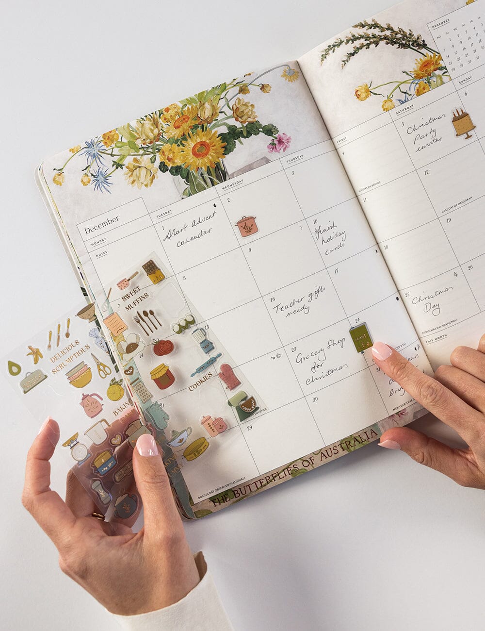 Calendar with floral and decorative elements held by hands on a light background