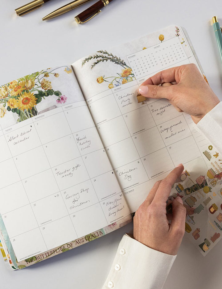 Person using a planner with floral and travel-themed design on a light surface.