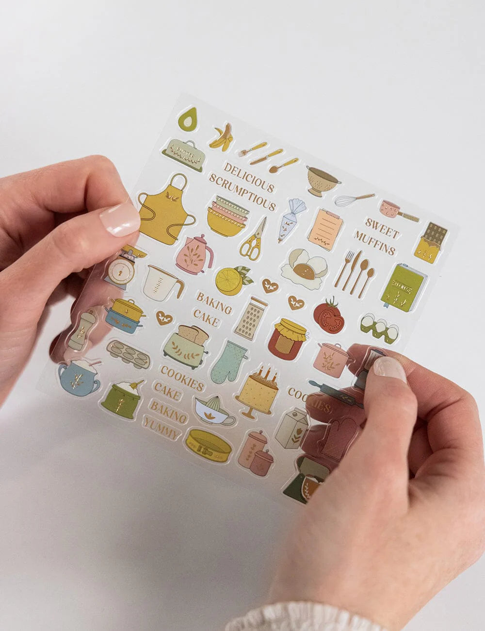 Sheet of baking-themed stickers held by hands against a white background