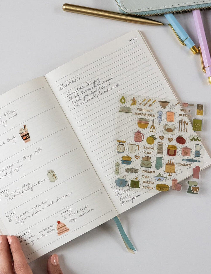Open notebook with recipe notes and decorative stickers on a white surface
