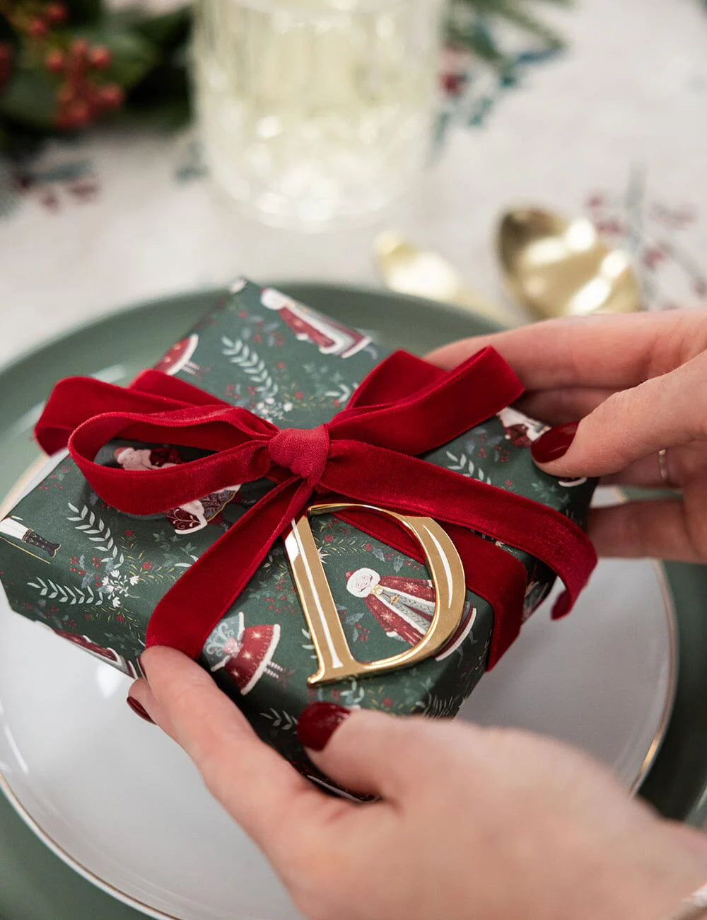 Gift box with red ribbon and gold letter 'D' being held on a table.