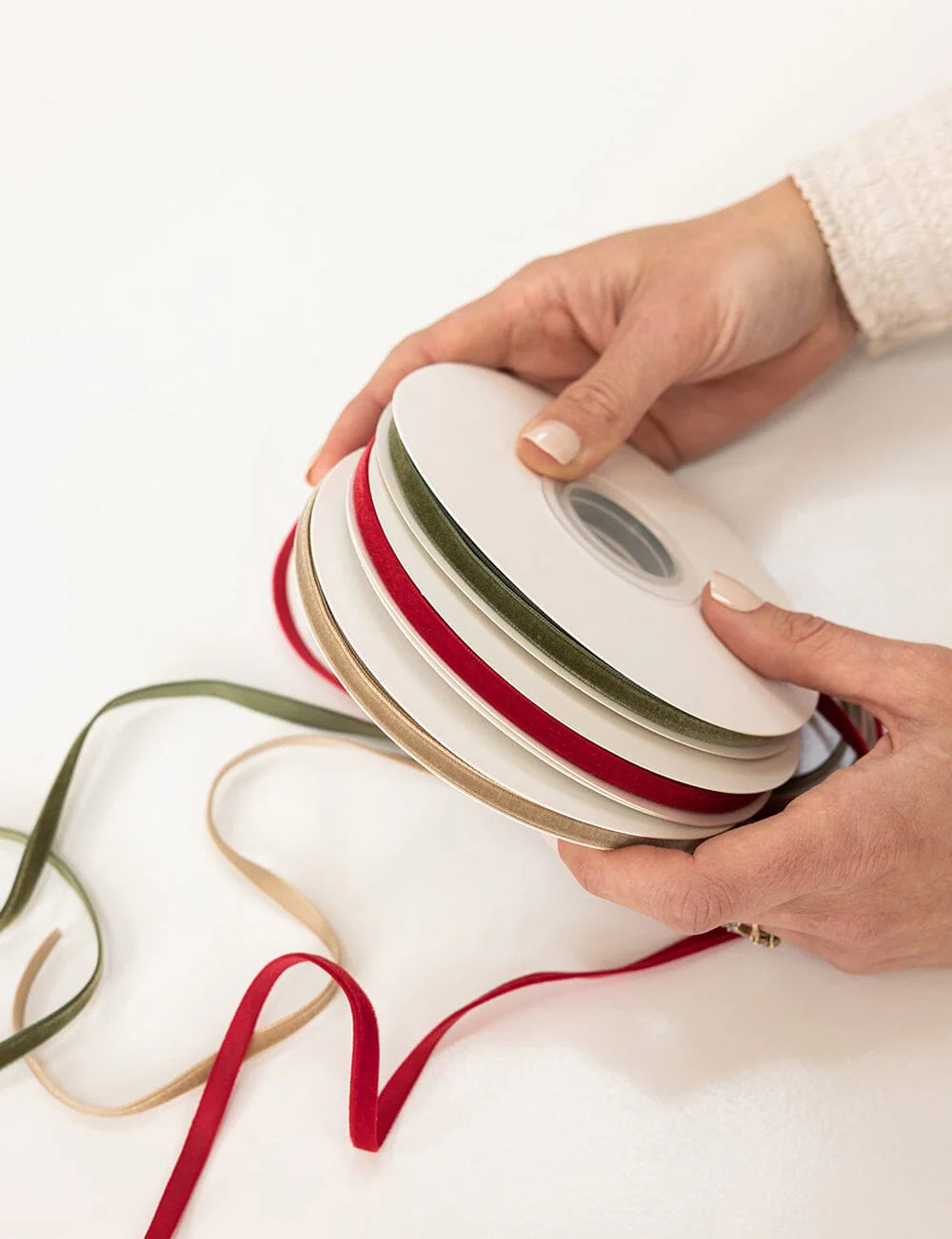 Person holding a spool of red, green, and white ribbon on a white background