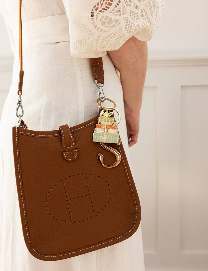 Brown leather handbag with a decorative keychain held by a person wearing a white dress.