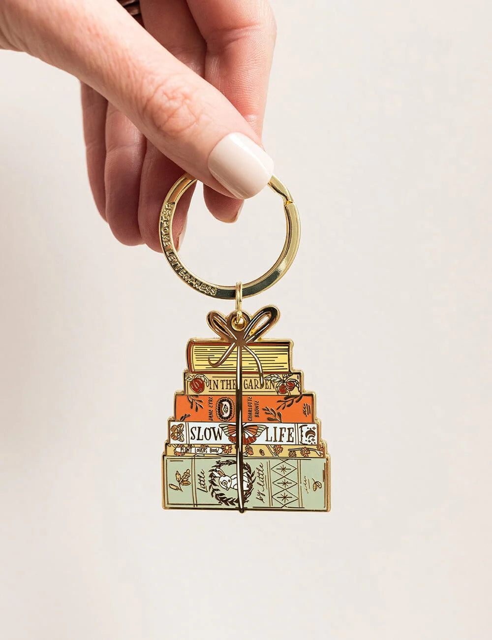 Keychain with stacked books design held by a hand against a plain background