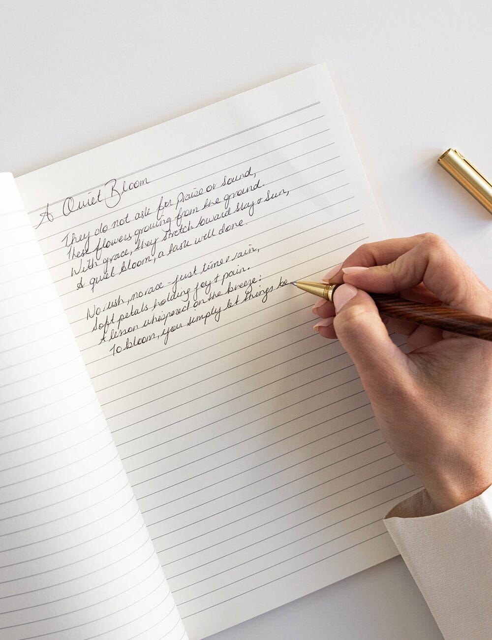 Hand writing in a notebook with a gold pen on a white surface