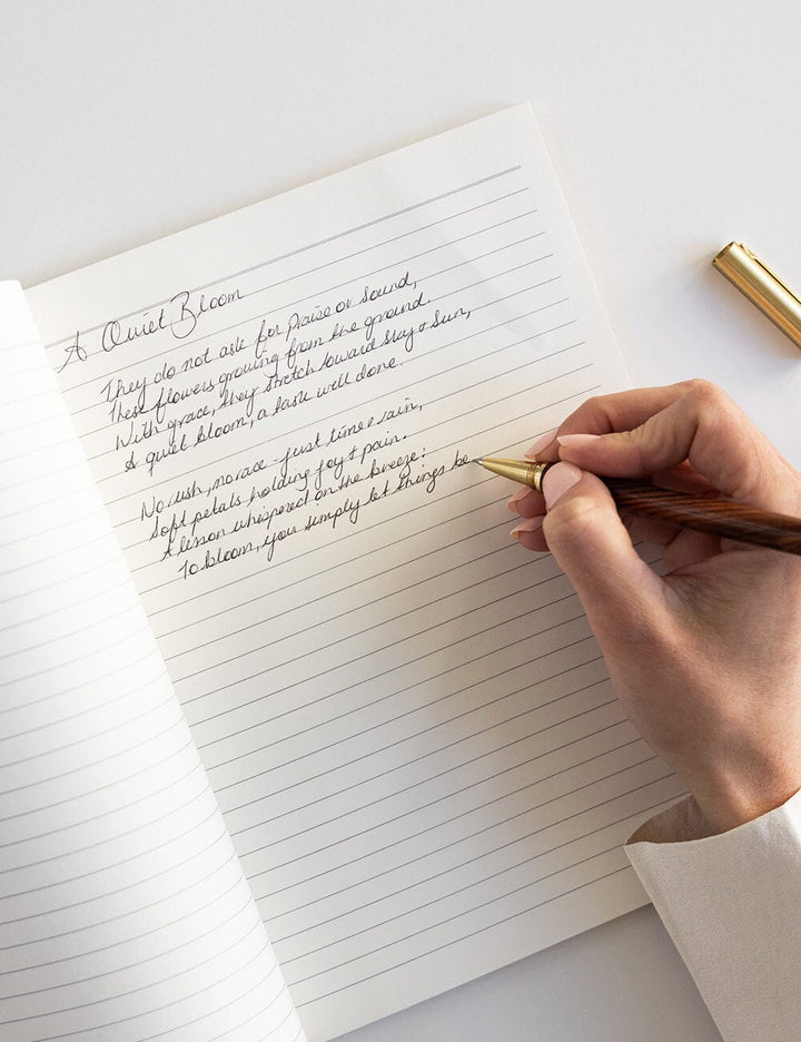 Hand writing in a notebook with a gold pen on a white surface