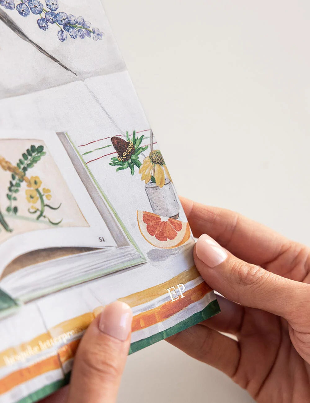 Hand holding a small notebook with a colorful design, featuring a drink illustration.