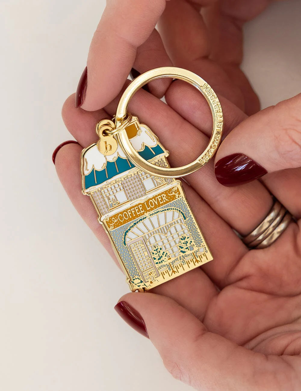 Gold keychain shaped like a coffee shop with 'Coffee Lover' text held by a hand.