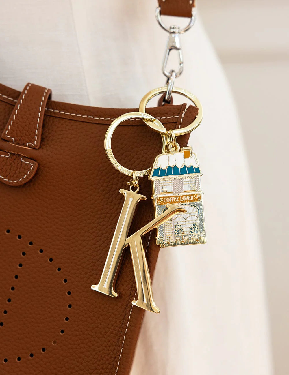Keychain with a gold letter 'K' and a small bag charm attached to a brown leather bag.