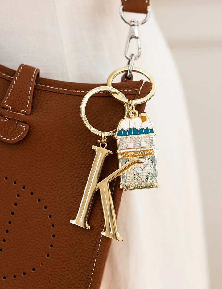Keychain with a gold letter 'K' and a small bag charm attached to a brown leather bag.