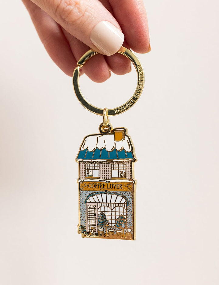 Keychain shaped like a coffee shop with 'Coffee Lover' text, held by a hand on a light pink background.