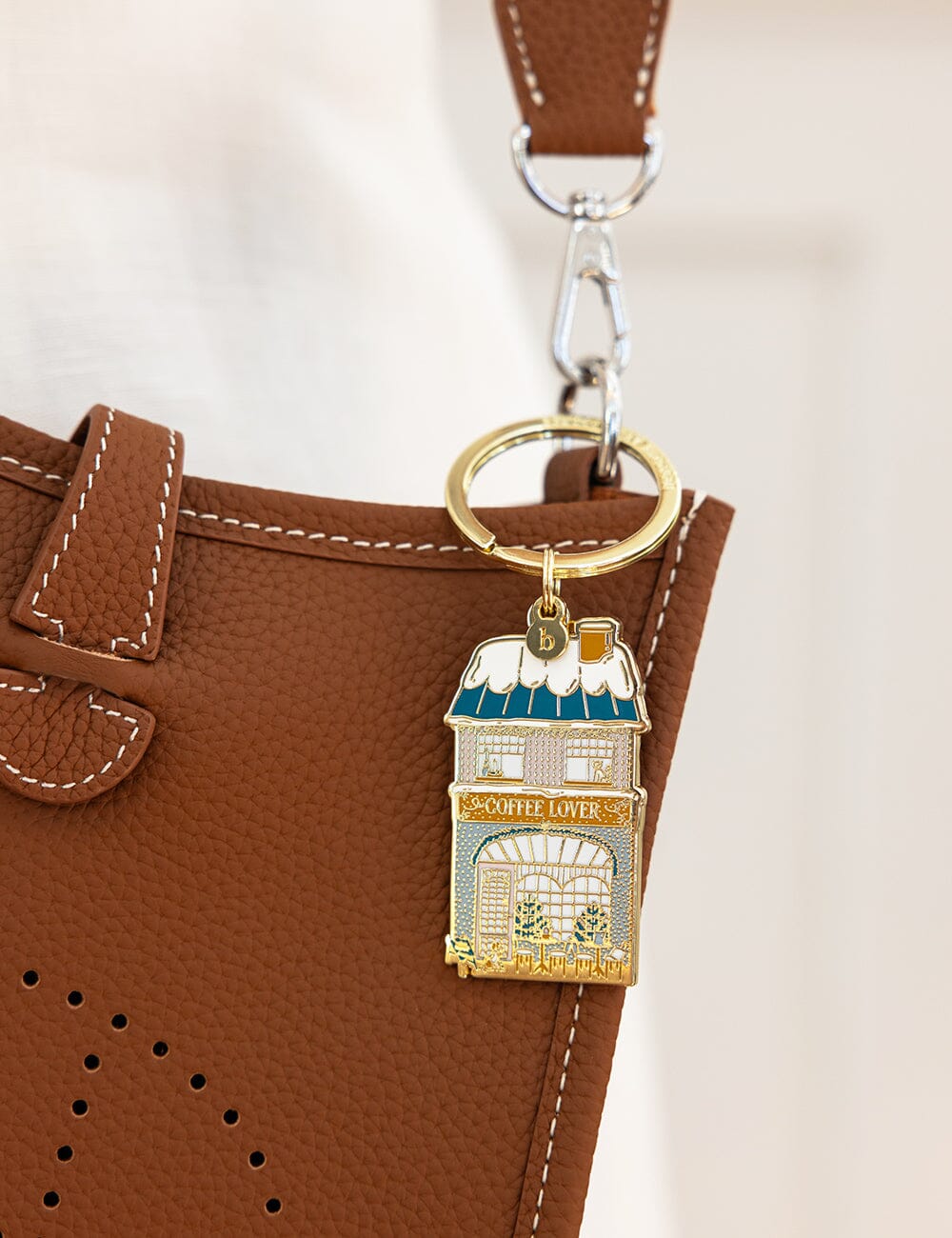 Keychain with coffee shop design attached to a brown leather bag.