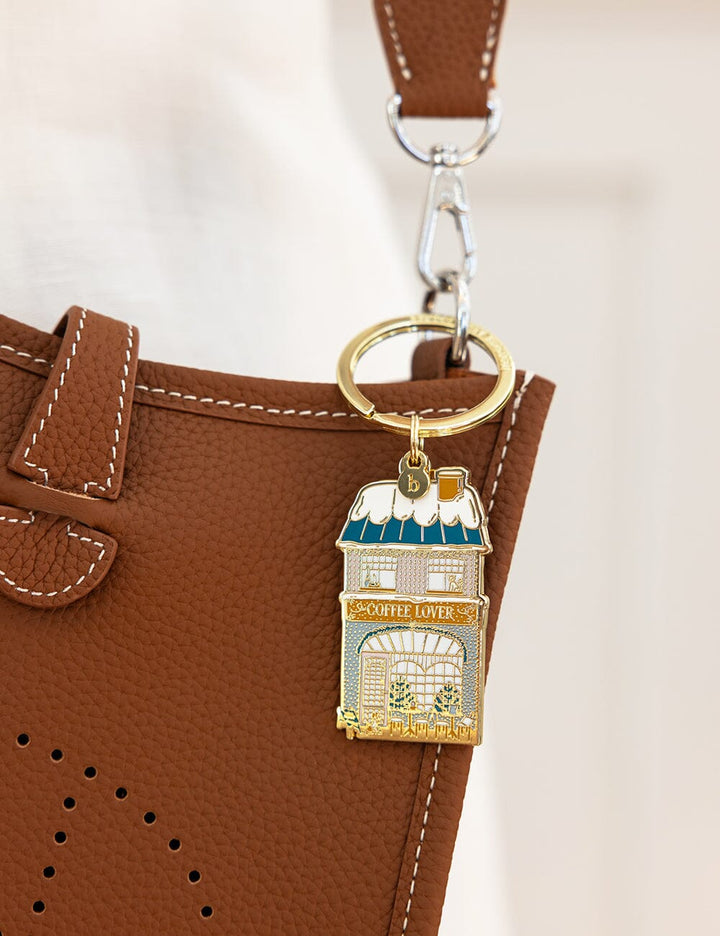 Keychain with coffee shop design attached to a brown leather bag.