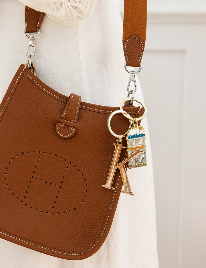 Brown leather handbag with a keychain featuring a letter 'K' on a light background