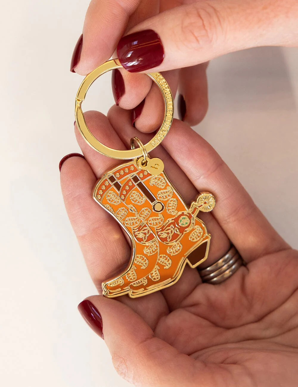 Hand holding a gold and orange boot-shaped keychain against a white background