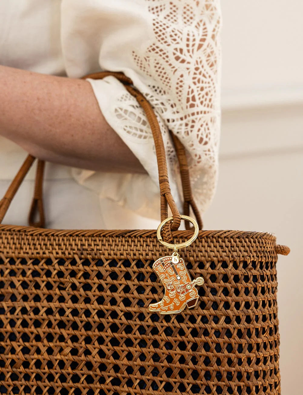 Brown woven handbag with a cowgirl boot keychain on a neutral background