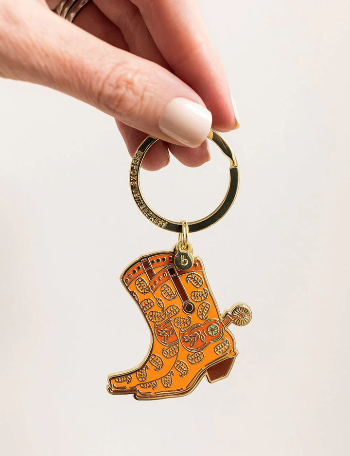 Orange boot-shaped keychain held by a hand against a light background
