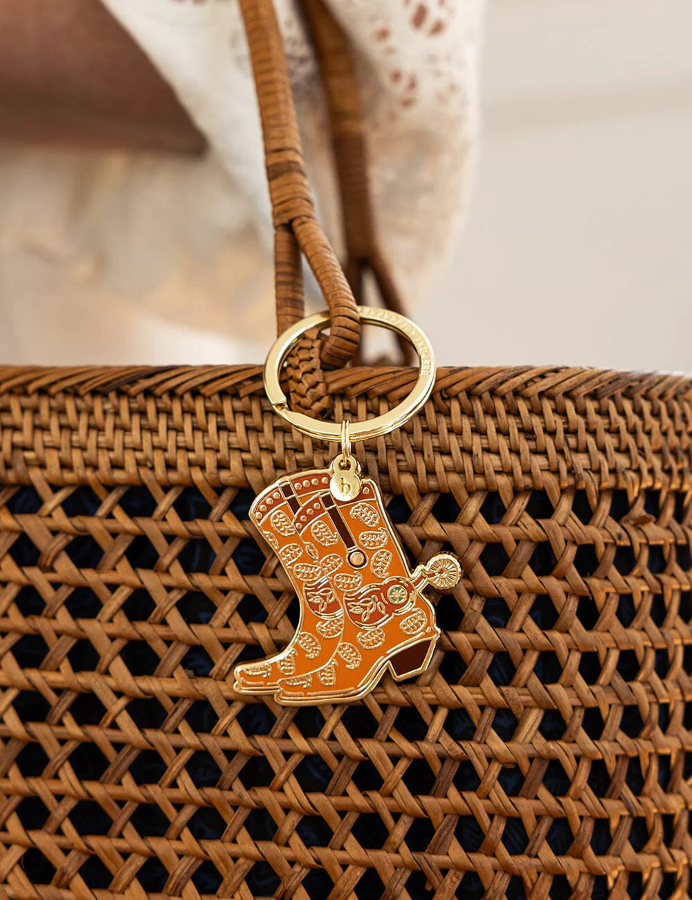 Brown woven handbag with a cowgirl boot keychain on a blurred background