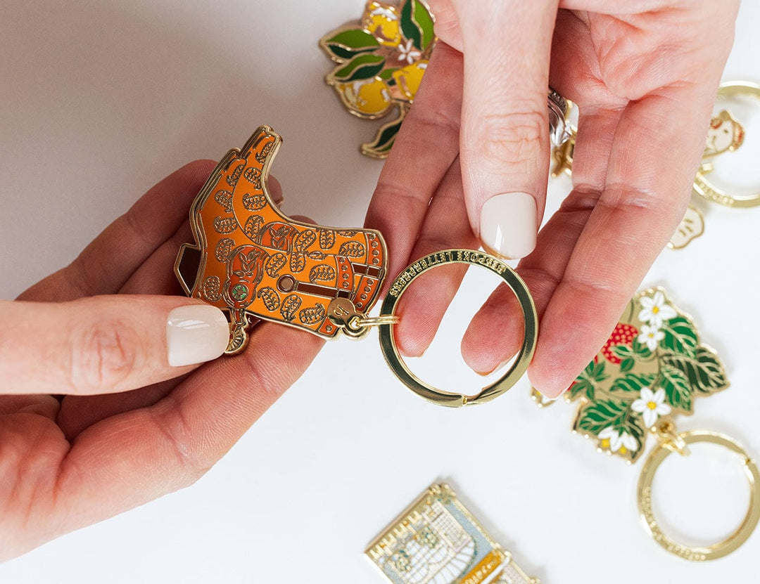 Hand holding a yellow boot-shaped keychain with other keychains in the background.