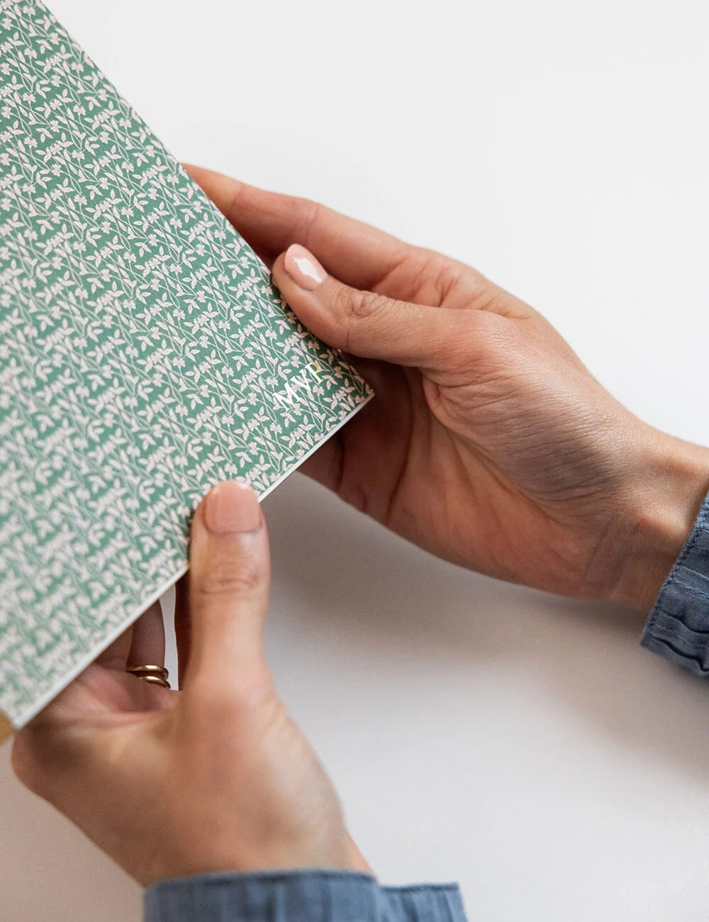 Person holding a green notebook with a white pattern on a light background